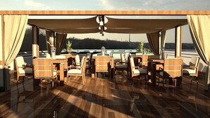 Un espacio al aire libre techado con mobiliario de madera y vistas a un cuerpo de agua.