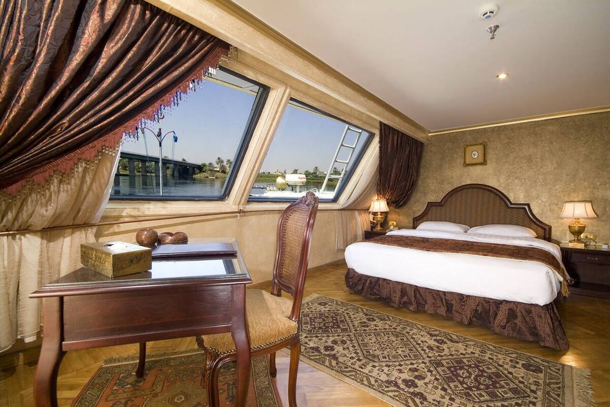 Une chambre d’hôtel avec un grand lit, un bureau avec une chaise, une fenêtre avec des rideaux et une vue sur un pont.