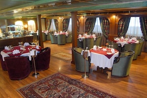 A restaurant with multiple tables set for dining, featuring red tablecloths and green upholstered chairs. - SUNRISE Terramar Cruise (Luxor)