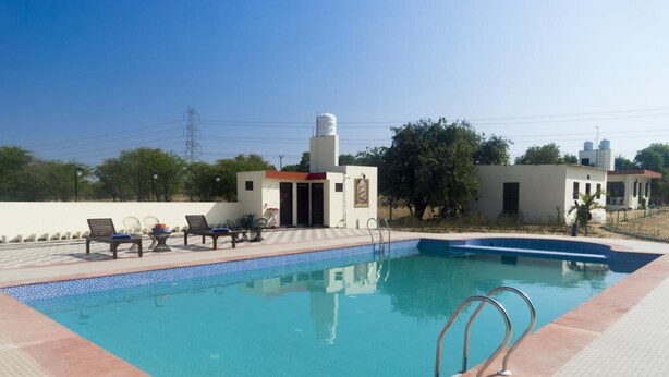 A swimming pool with lounge chairs and a small building with a water tank. - Vacation Village Luxury Tent - A Unit Of Braham Vatika Resort (Pushkar)