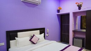 A hotel room with a bed, a small desk, a phone, and a shelf with flowers. - Vacation Village Luxury Tent - A Unit Of Braham Vatika Resort (Pushkar)