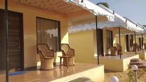 A hotel with a covered outdoor seating area, wicker chairs, and a tiled floor. - Vacation Village Luxury Tent - A Unit Of Braham Vatika Resort (Pushkar)