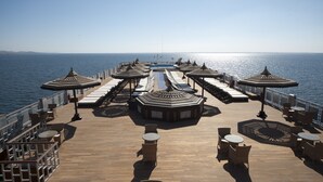 Une terrasse ensoleillée, dotée de chaises longues et de parasols, avec vue sur la mer.