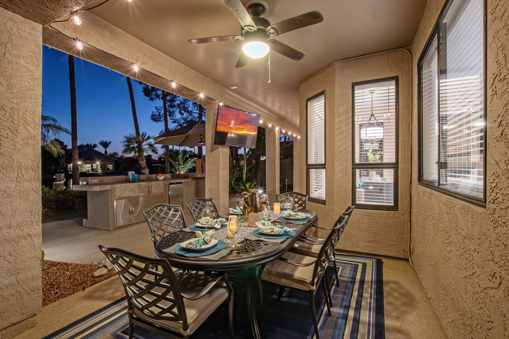 An outdoor dining area with a ceiling fan, string lights, and a TV screen.