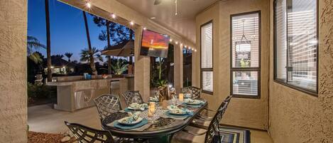 An outdoor dining area with a ceiling fan, string lights, and a TV screen.