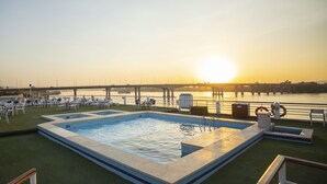 A pool area with chairs and a lifebuoy, overlooking a river with a bridge in the background. - SUNRISE Semiramis I Cruise (Luxor)