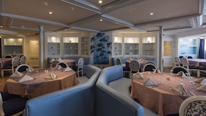 A restaurant with round tables, blue cushioned booths, and white chairs. - SUNRISE Semiramis I Cruise (Luxor)