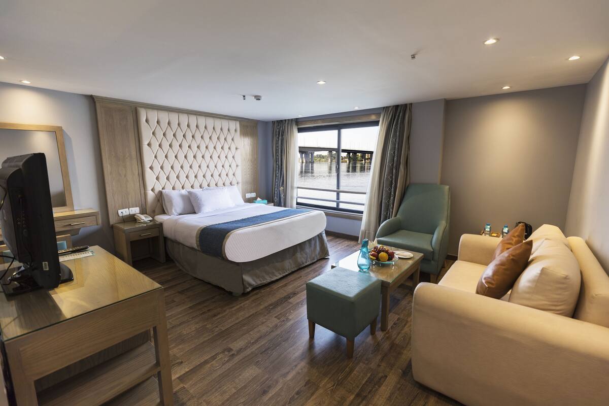 A hotel room with a bed, a desk with a computer, a sofa, and a view of a body of water.