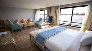A hotel room with a large bed, a sofa, a TV, and a view of the water. - SUNRISE Semiramis I Cruise (Luxor)