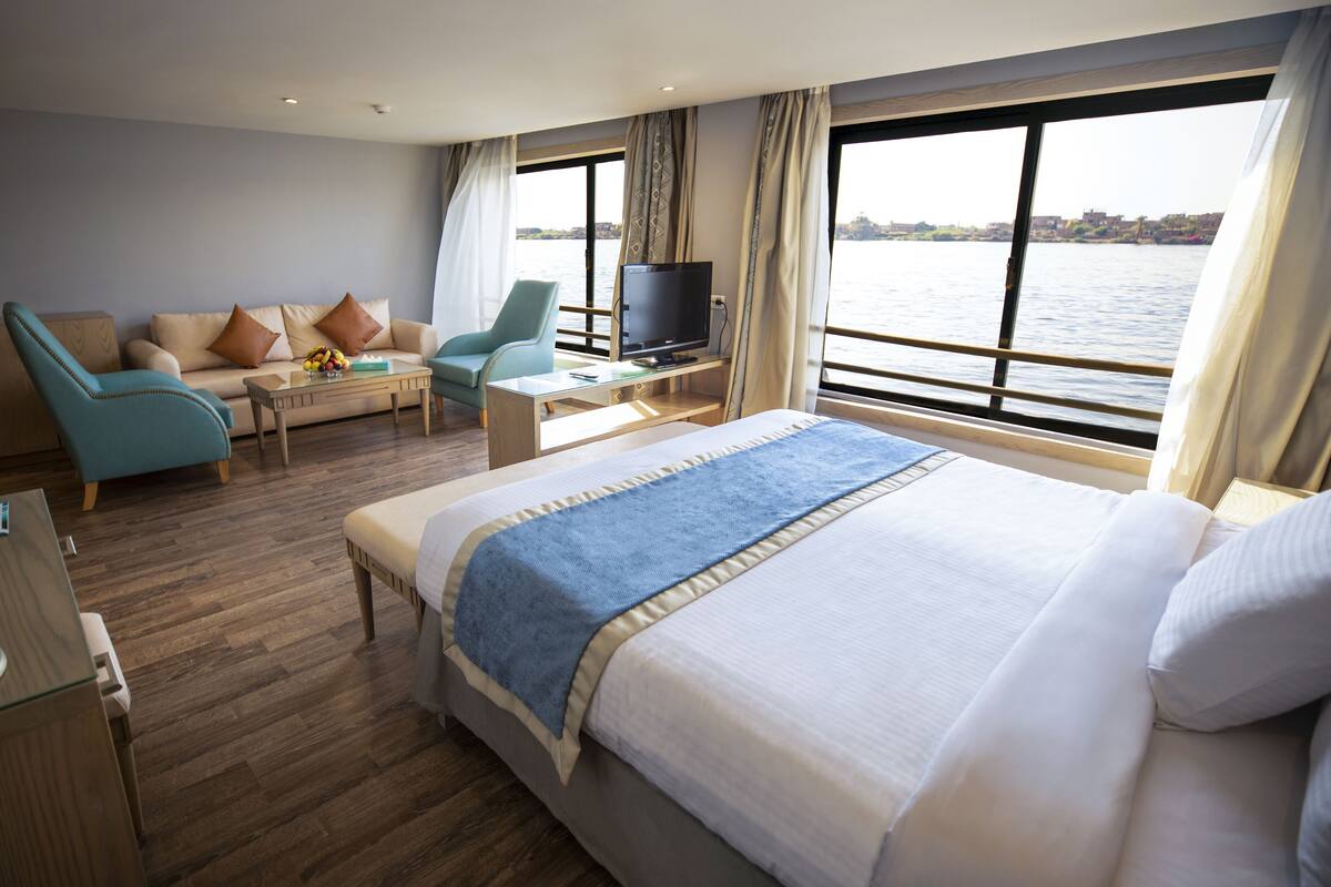 A hotel room with a large bed, a sofa, a TV, and a view of the water.