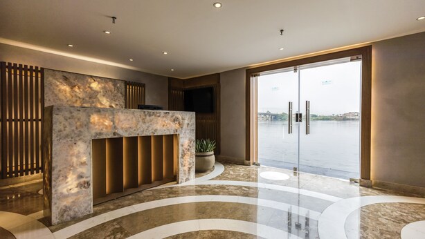 A modern lobby with a marble reception desk, a large glass door leading outside, and a potted plant. - SUNRISE Semiramis II Cruise (Luxor)