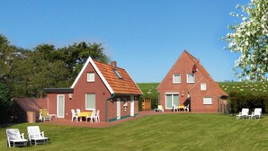 Uma casa de dois andares com fachada de tijolos vermelhos e telhado inclinado. Há um pátio com móveis de jardim e um gramado em primeiro plano.