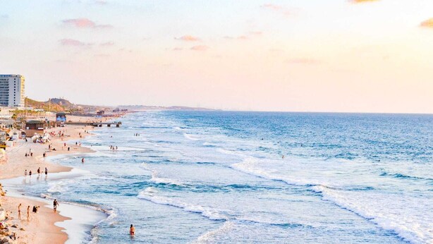 A beach with people walking along the shore and a pier extending into the water. - Charming 3bdr apt with sea view B5 (Bat Yam)