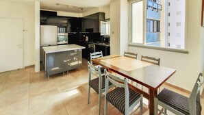 A modern kitchen with a dining area, including a table and chairs, and a large window providing a view of the building outside. - Charming 3bdr apt with sea view B5 (Bat Yam)