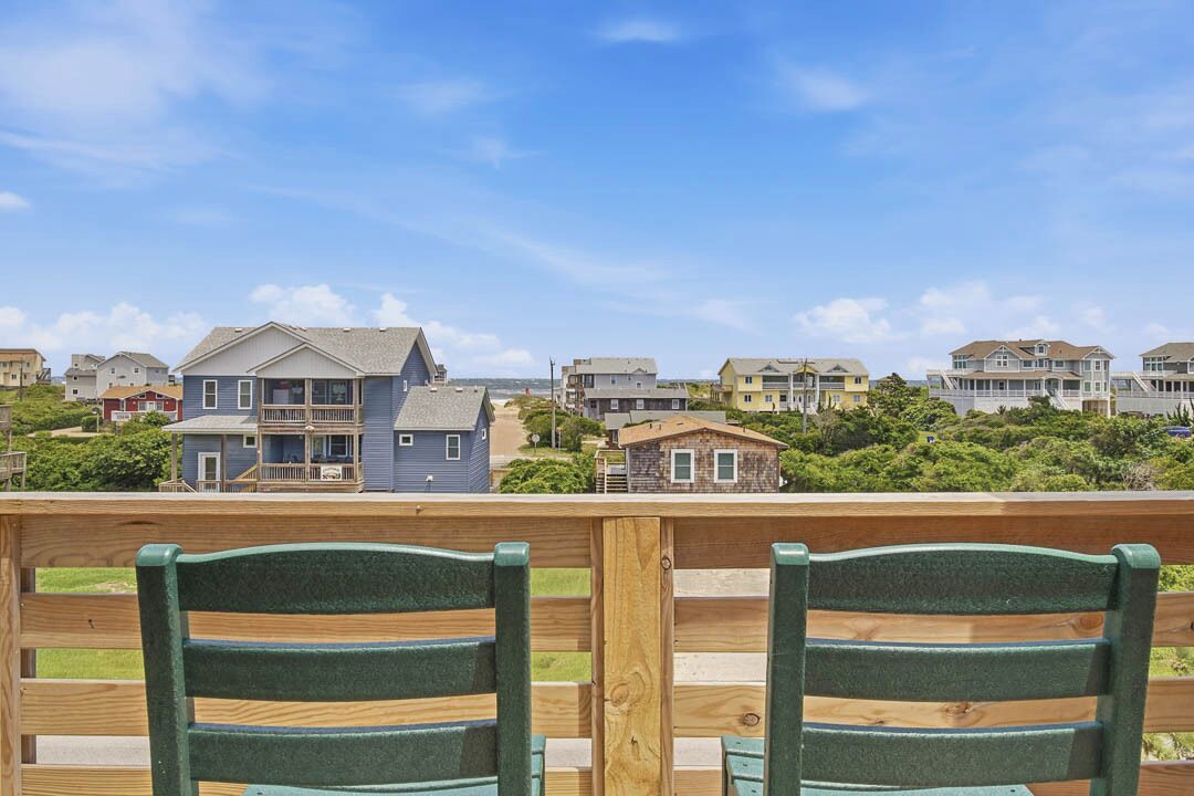 Une terrasse en bois avec deux chaises vertes, une vue sur des maisons et un ciel dégagé.
