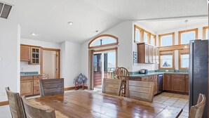 A spacious kitchen with wooden cabinets, a large dining table, and a view through an archway. - The After Glow | 940 ft from the beach | Private Pool, Hot Tub (Nags Head)