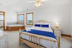 A bedroom with a bed, a wooden headboard, a nightstand, a lamp, a ceiling fan, and a bathtub.