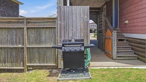 Un patio trasero con una parrilla, cerca de madera y una casa de fachada roja.