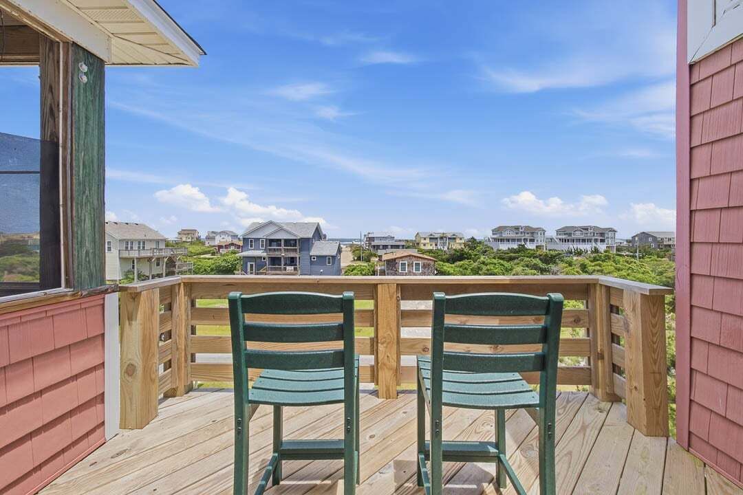 Une terrasse en bois avec deux chaises vertes, donnant sur un quartier résidentiel avec des maisons et de la verdure.