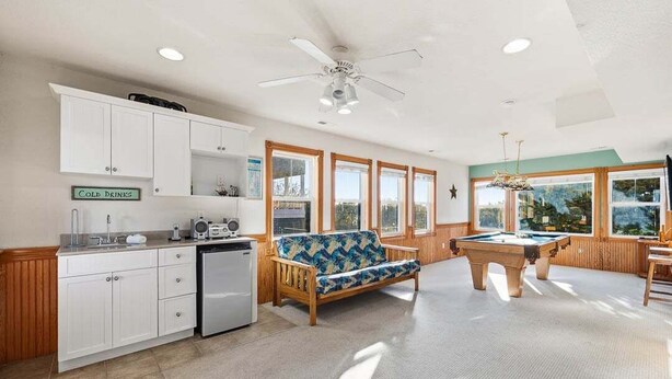 Un amplio salón con mesa de billar, un sofá y una zona de cocina con refrigerador y armarios.