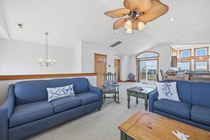 Een ruime woonkamer met een blauwe bank, een houten salontafel en een plafondventilator.