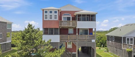A multi-story building with a balcony on the upper floor, a covered entrance, and a small outdoor area with a tree.