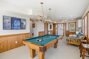A pool table with balls, a sofa, and a ceiling fan in a room with wooden paneling and a framed picture on the wall. - The After Glow | 940 ft from the beach | Private Pool, Hot Tub (Nags Head)