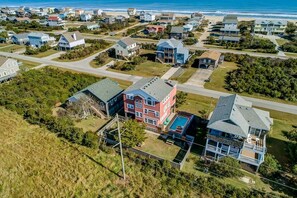 An aerial view of a residential area with houses, a swimming pool, and a beach in the background. - The After Glow | 940 ft from the beach | Private Pool, Hot Tub (Nags Head)
