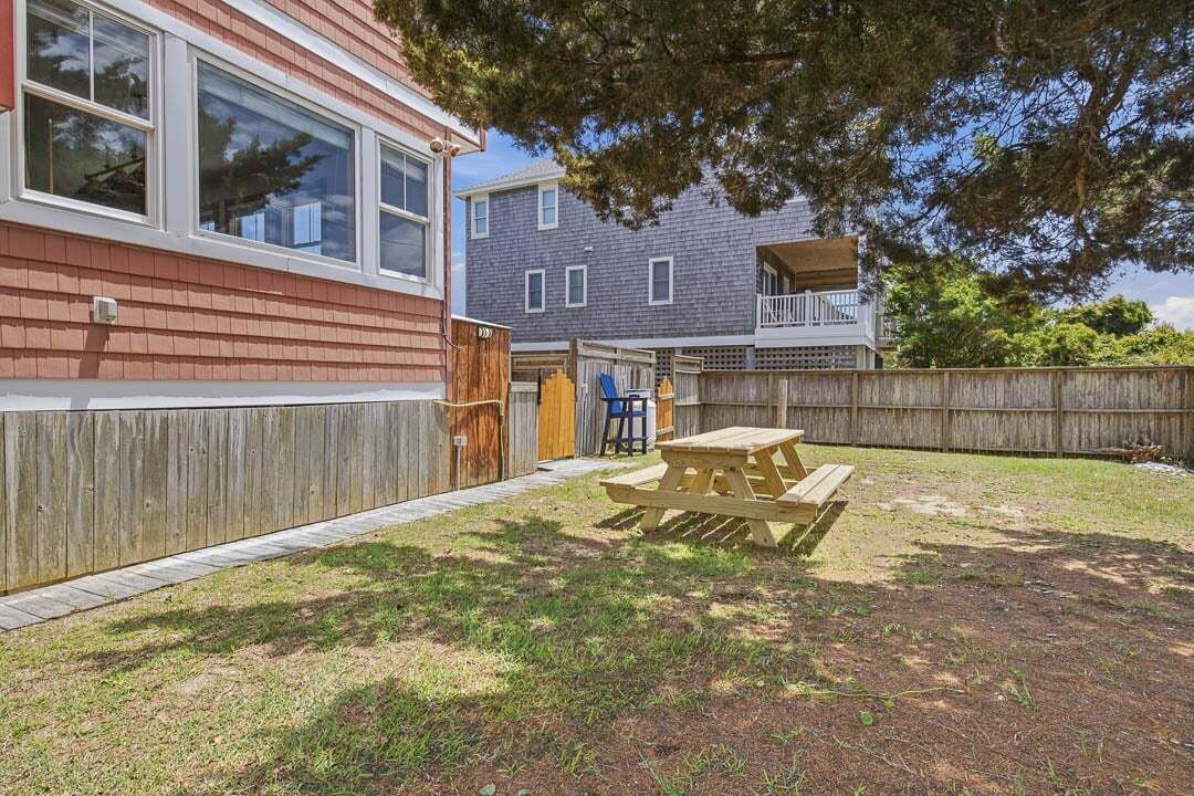 A residential backyard with a wooden fence, a picnic table, and a house with a red exterior and large windows.