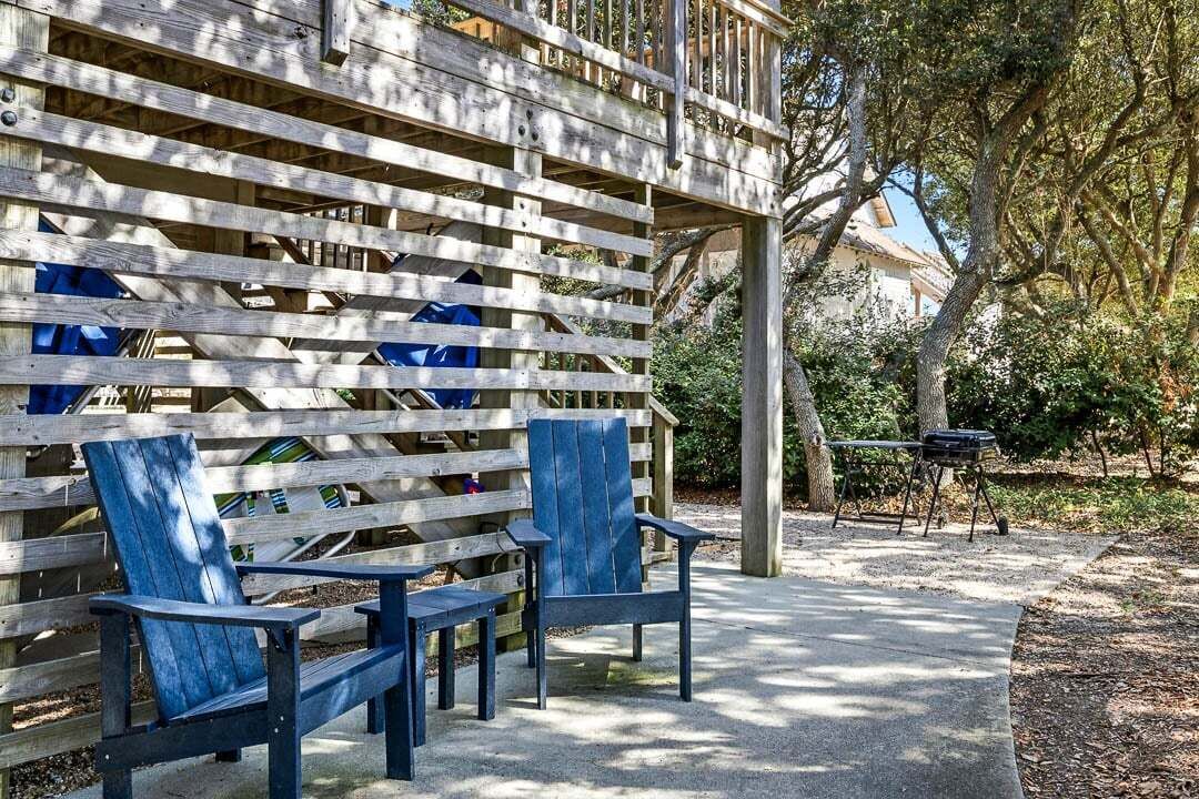 A wooden deck with two blue Adirondack chairs, a barbecue grill, and a covered area with a wooden railing.