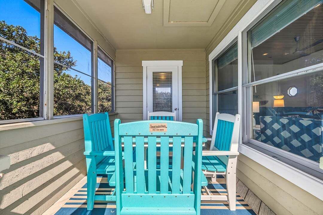 A covered porch with turquoise chairs and a table, a door, and large windows.