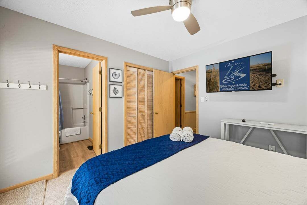 A bedroom with a bed, a ceiling fan, a TV, and a wooden wardrobe.