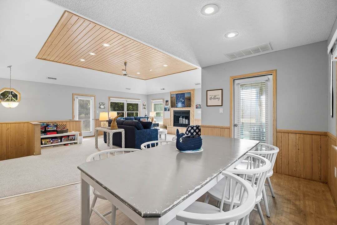 Un vaste espace de vie doté d’un plafond en bois, d’une table à manger avec des chaises, d’un canapé et d’une bibliothèque.