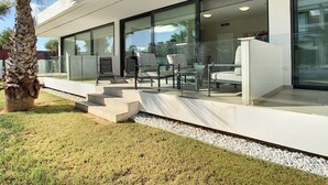 Um pátio moderno ao ar livre com paredes de vidro, uma palmeira e móveis de exterior.
