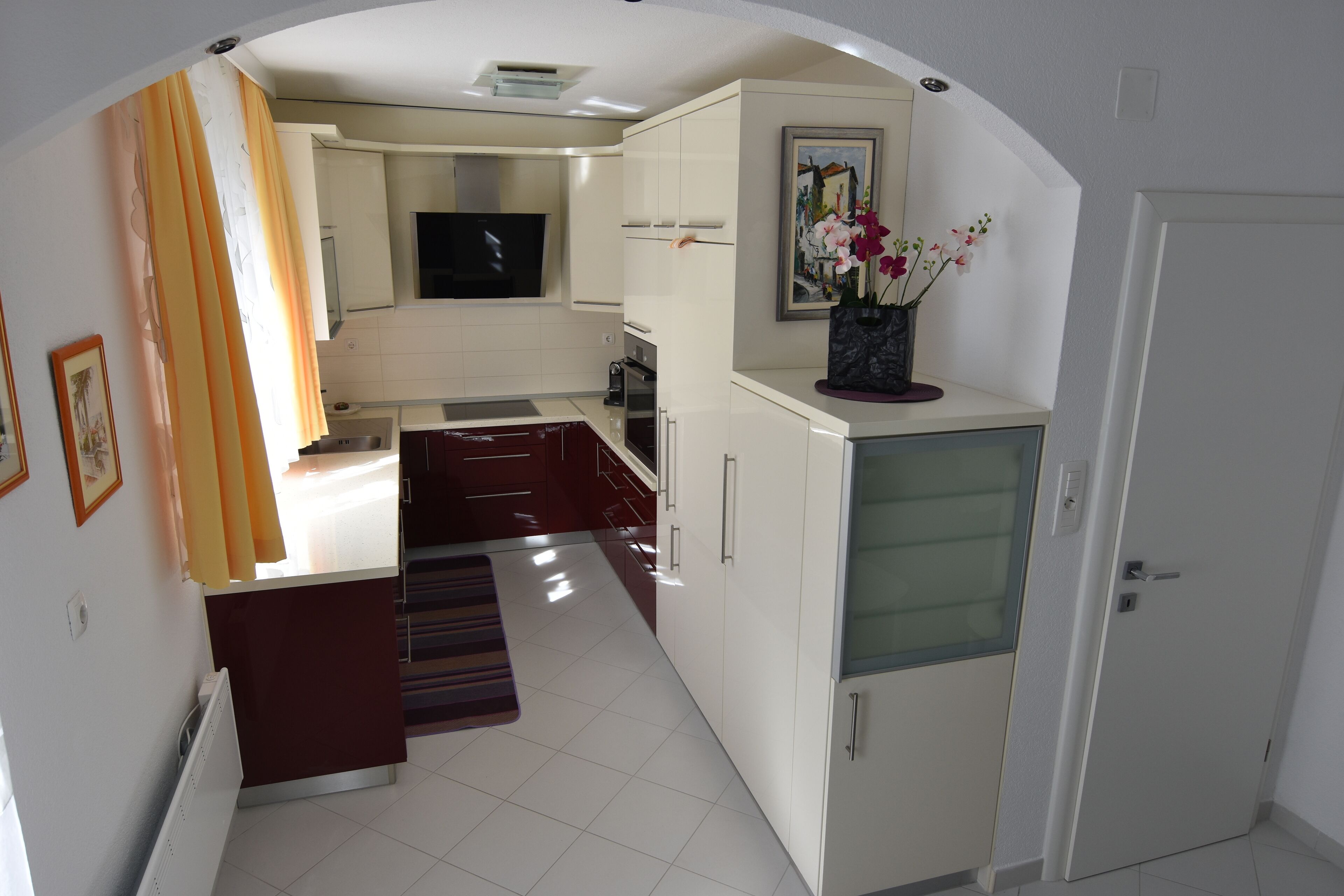 Una cocina moderna con armarios blancos, horno empotrado y televisor sobre la encimera.