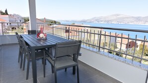 A balcony with a table and chairs, overlooking a scenic view of a body of water and distant hills. - Villa Portofino (Okrug)