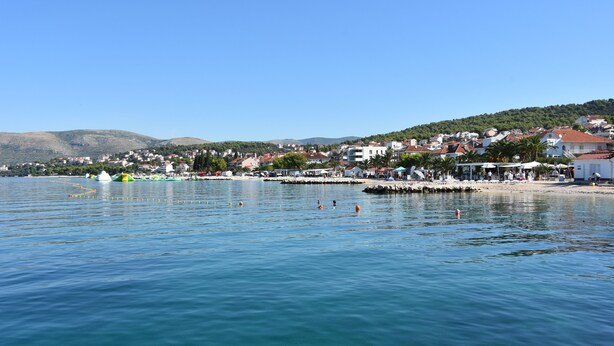 A coastal town with buildings along the waterfront, calm water, and hills in the background. - Villa Portofino (Okrug)