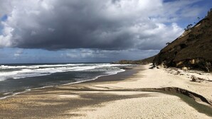 Une plage avec une falaise rocheuse et des vagues.