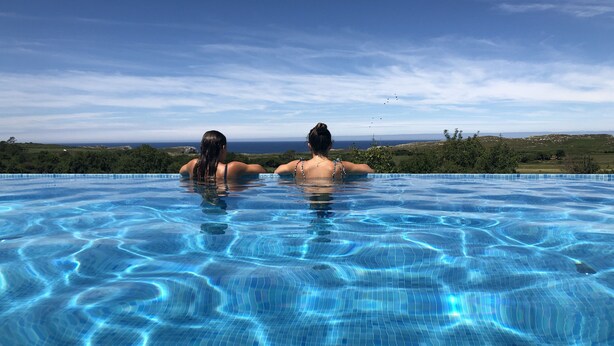 Une piscine où se trouvent deux personnes, entourée d’un paysage magnifique et sous un ciel dégagé.