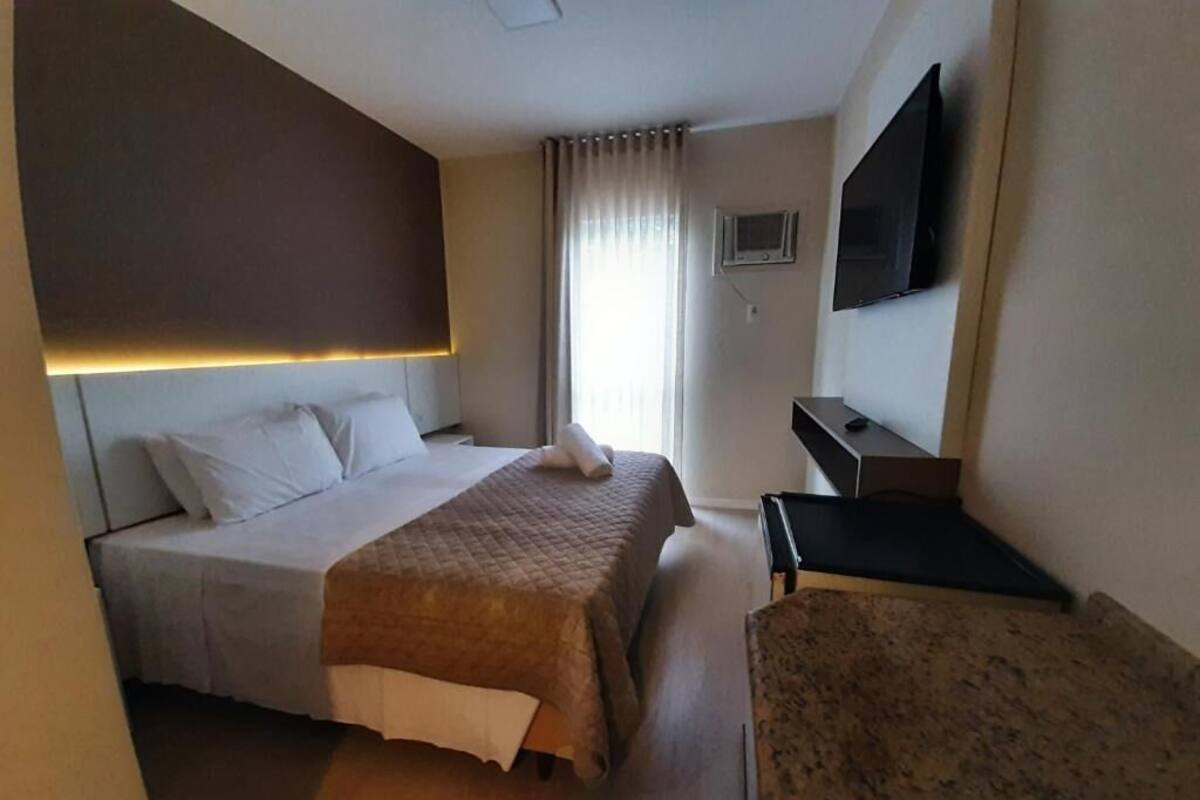 A hotel room with a bed, a desk, a chair, a TV, and a window with curtains.