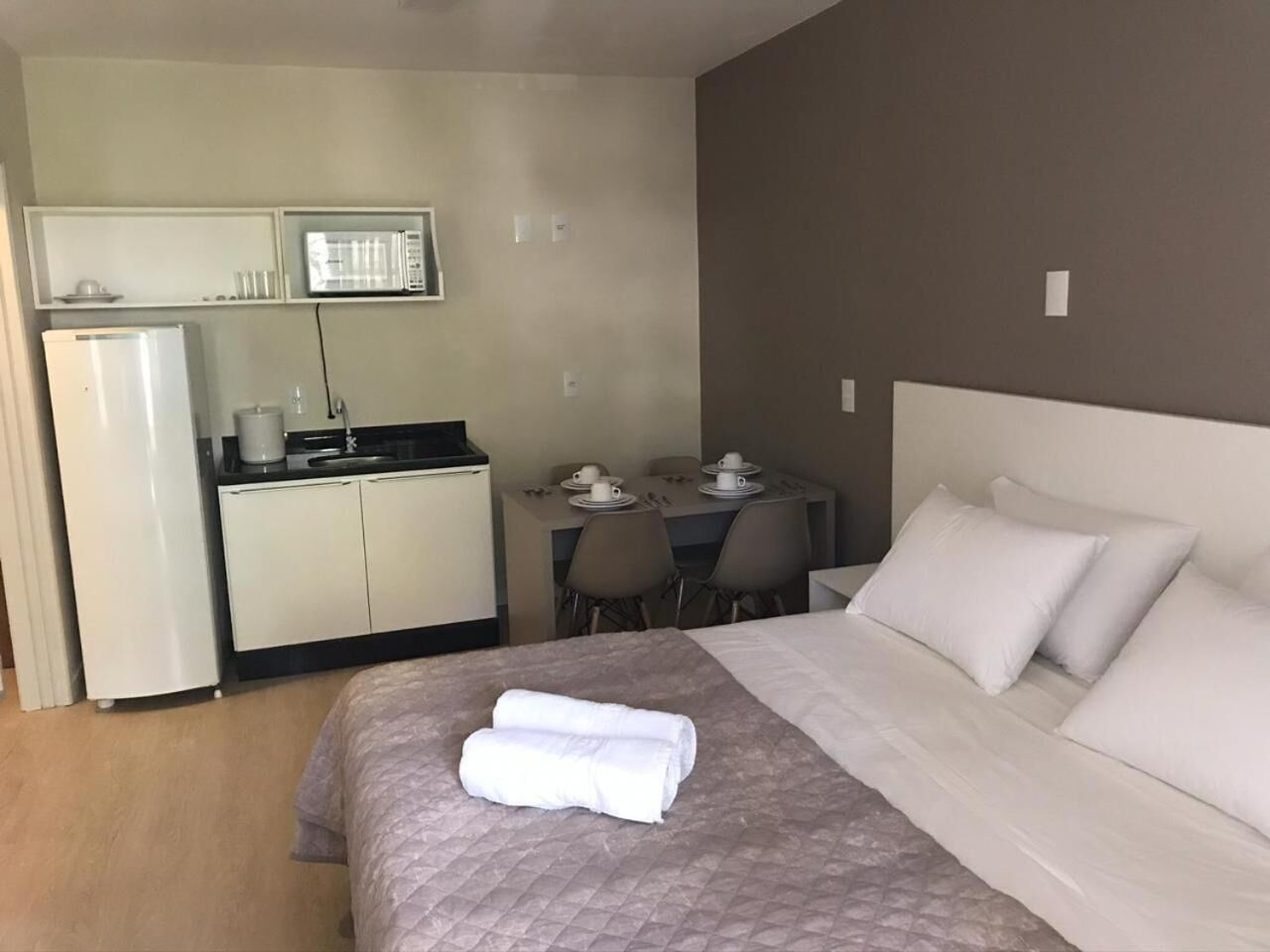 A hotel room with a bed, a desk with chairs, a microwave, and a refrigerator.