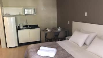 A hotel room with a bed, a desk with chairs, a microwave, and a refrigerator.