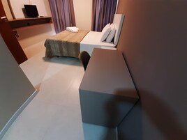 Una camera d'albergo moderna con un letto, una scrivania e un televisore su uno scaffale.