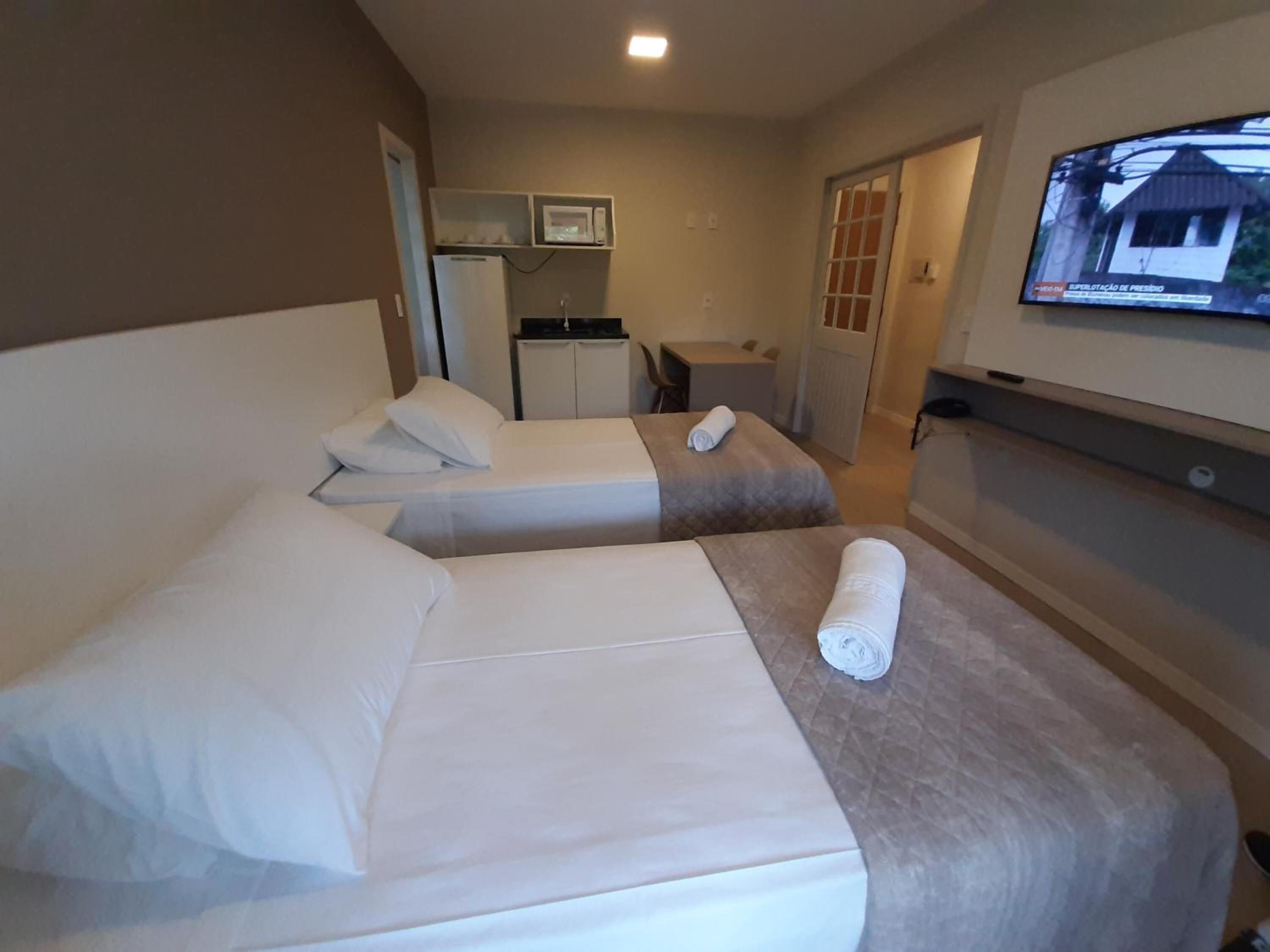 A hotel room with two beds, a small kitchenette, a TV, and a bathroom visible through an open door.