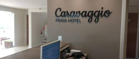 A reception desk with a computer, a phone, and a sign that reads "Caravaggio Praia Hotel".