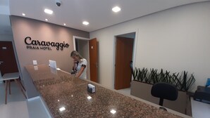 Mostrador de recepción en el Caravaggio Praia Hotel, con un recepcionista, una planta y un diseño de interiores moderno.
