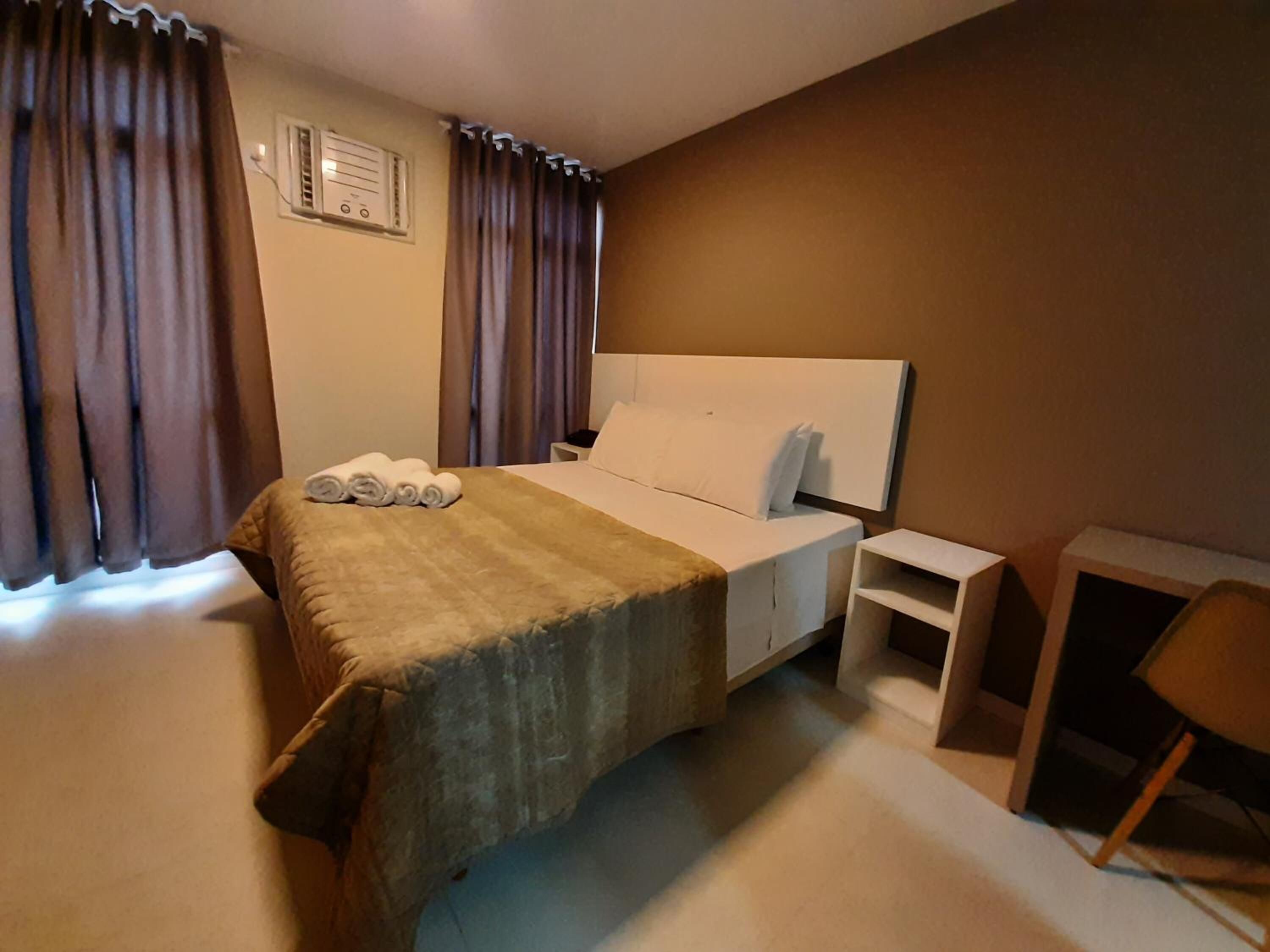 A hotel room with a bed, a nightstand, a chair, and curtains.