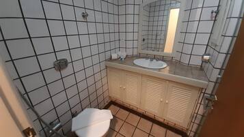 Un baño con inodoro, lavamanos, espejo y paredes de azulejos.