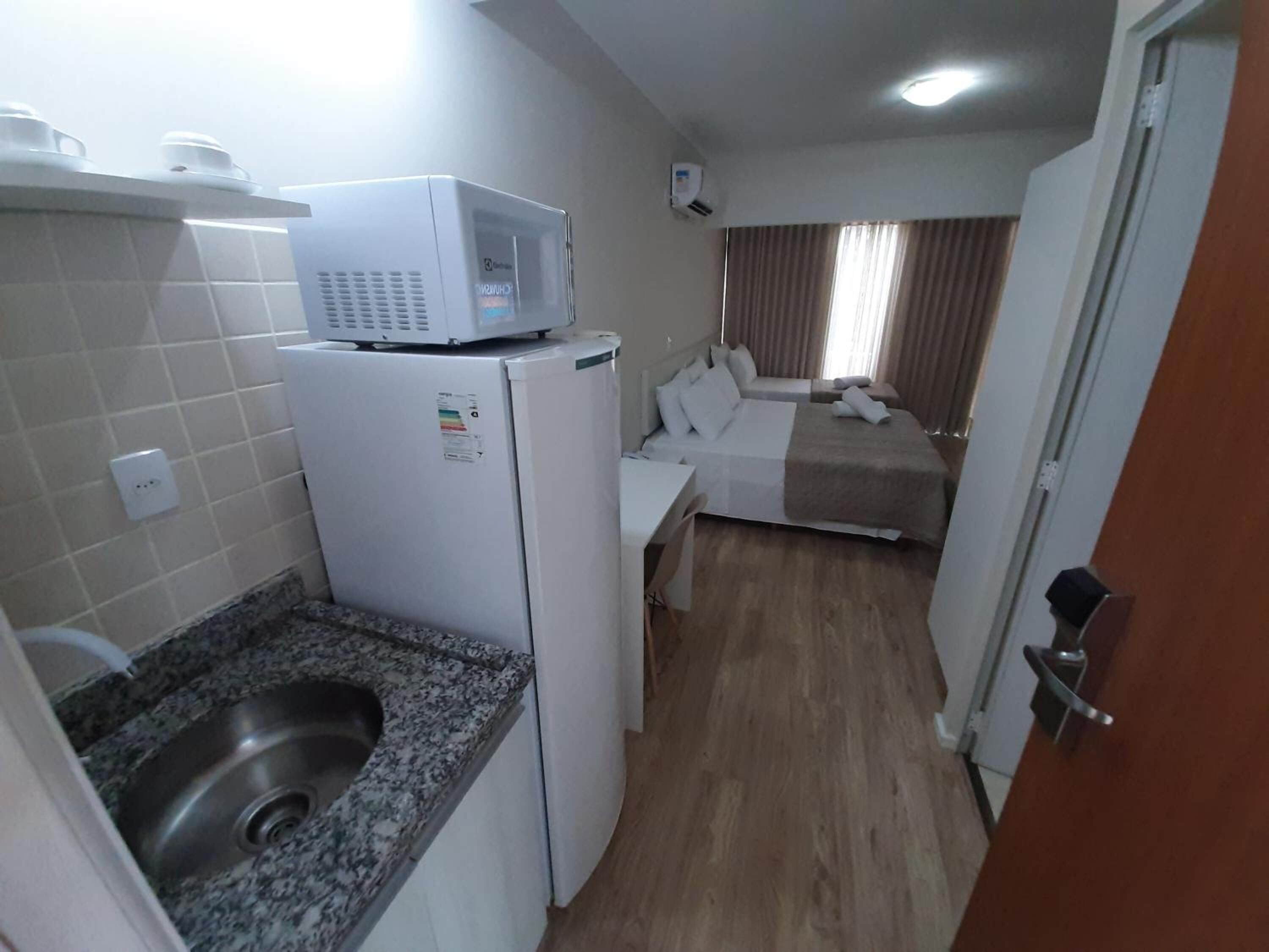 A compact hotel room with a kitchenette, a bed, and a bathroom.