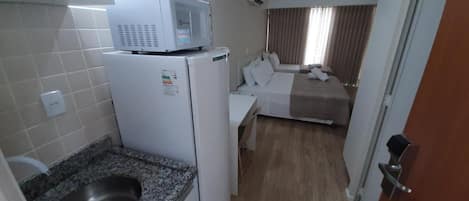 A compact hotel room with a kitchenette, a bed, and a bathroom.